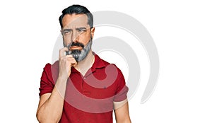 Middle aged man with beard wearing casual red t shirt serious face thinking about question with hand on chin, thoughtful about