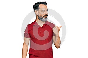 Middle aged man with beard wearing casual red t shirt smiling with happy face looking and pointing to the side with thumb up