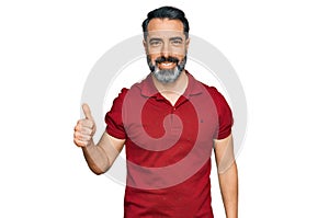 Middle aged man with beard wearing casual red t shirt smiling happy and positive, thumb up doing excellent and approval sign