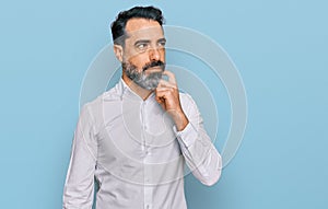 Middle aged man with beard wearing casual white shirt serious face thinking about question with hand on chin, thoughtful about