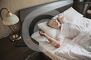 A middle-aged man in bed in his bedroom wakes up in the morning with a smile on his face. The concept of healthy sleep