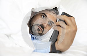 Middle aged man in bed, lookingat his phone, social media addiction