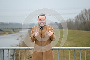 Middle aged man on a bridge giving thumbs up gesture