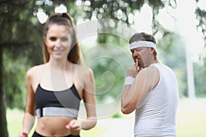 Middle aged man check on young beautiful fit woman running in park