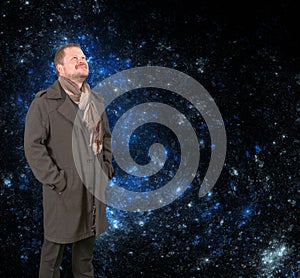 Middle-aged man in a coat looking up on starry universe background