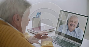 Middle-aged man is communicating with his elderly father by online video call on laptop, staying home