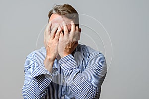 Middle aged man covering his face with his hands