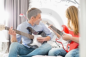 Middle-aged man with daughter playing guitars at home