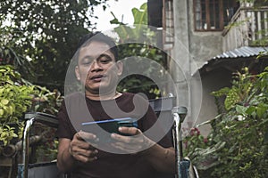 A middle aged man with a disability caused by childhood polio checks his social media on his cellphone while outside his house