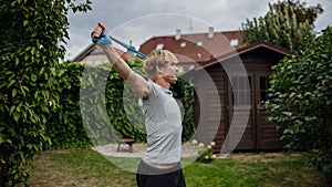 Middle aged man doing strength exercises with resistance band outdoors in garden. Concept of workout routine at home.