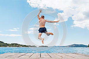 Middle-aged man dressed swimming trunks funny jumping to the waves from the boat pier as he having fun on merry vacation days on