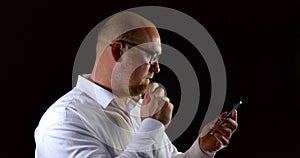 Middle aged man dressed in white shirt is holding mobile phone in hands and checking email