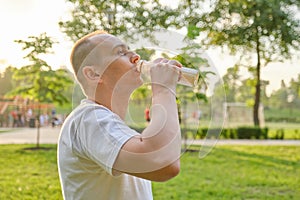 Middle-aged man drinking milk, dairy product from bottle outdoor