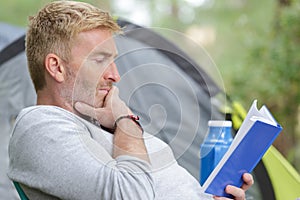 Middle-aged man engrossed in book by tent photo