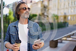 Middle aged man got distracted from mobile phone enjoying coffee outdoors looking at sunset. Middle aged man looking