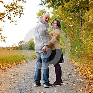 Middle-aged man in a gray sweater and a woman in a yellow stand, embracing, in an autumn park against the background of trees, the