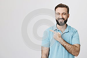 Middle aged man with a happy smile pointing away over white background. Handsome bearded guy just saw how his friend