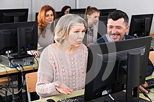 Middle aged man helping woman to use computer