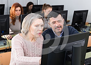 Middle aged man helping woman to use computer