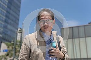 A middle aged man in his 40s looks taken aback while holding a cellphone in his hand. Outdoor city scene photo