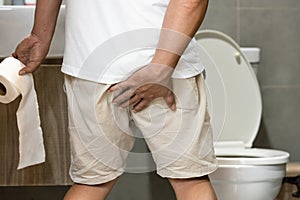 Middle aged man hold toilet paper,touching his butt worried about defecation fearing pain from hemorrhoids,Stressed male has acute