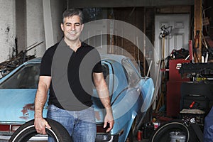 Middle aged man holding tire outside his garage.