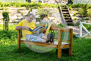 Middle aged man with laptop and documents working outside in garden, green home office concept