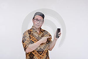 A middle aged man looking at the camera after checking his phone for new messages. Wearing a batik shirt and songkok skull cap.