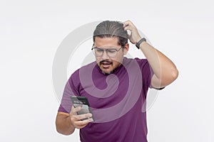 A middle aged man looking confounded and stumped, scratching his head while looking at his cellphone. Wearing eyeglasses and a photo