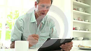 Middle Aged Man Looking At Digital Tablet Over Breakfast