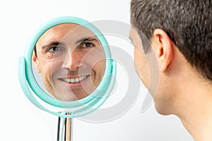 Middle aged man looking in hand mirror.