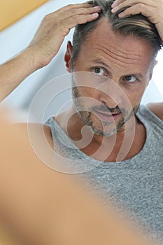 Middle-aged man looking at the mirror checking hair loss