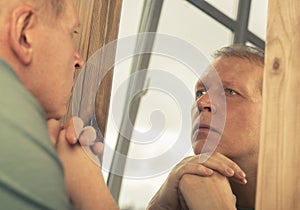 Middle-aged man looking at mirror reflection seriously, thinking about his age and life