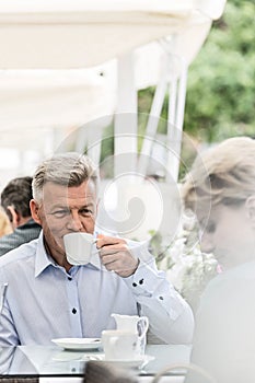 Middle-aged man looking at woman while having coffee at sidewalk cafe