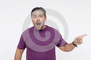 A middle aged man looks flabbergasted, looking at the camera while pointing to the right. Wearing a purple waffle shirt. Isolated