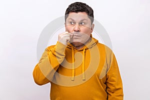 Middle aged man making zip gesture to close mouth, keeping secret, zipping lips.