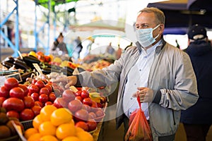 Middle aged man in mask buying tomatoes