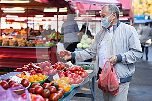 Middle aged man in mask buying tomatoes