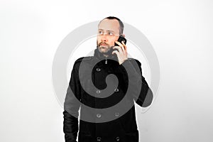 Middle-aged man with overcoat listens attentively to a conversation on his mobile phone, isolated on white