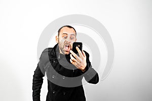 Middle-aged man with overcoat screams angrily at his mobile phone, isolated on white