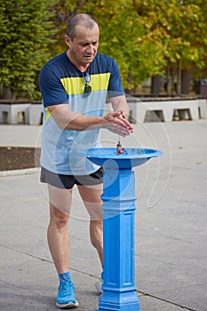 a middle-aged man in the park hydrating himself after a run