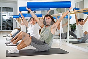 Middle-aged man practicing pilates with roller on gray mat in gym room