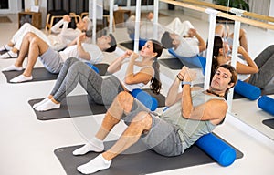 Middle-aged man practicing pilates with roller on gray mat in gym room