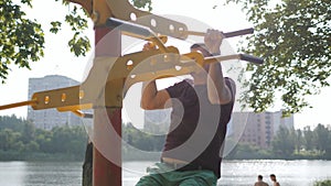 A middle-aged man pulls himself up on a horizontal bar on the sports ground. Outdoor sports in old age.