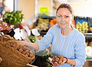 Middle-aged man purchaser taking walnuts from basket in greengrocery