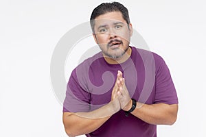 A middle aged man in a purple shirt saying sorry, with hands clasped. Isolated on a white background