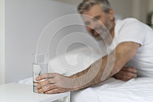 Middle aged man reaching glass of water on bedside table