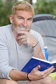 middle-aged man reading book by tent