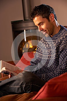 Middle Aged Man Relaxing With Book By Cosy Fire