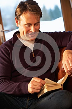 Middle Aged Man Relaxing With Book Sitting On Sofa